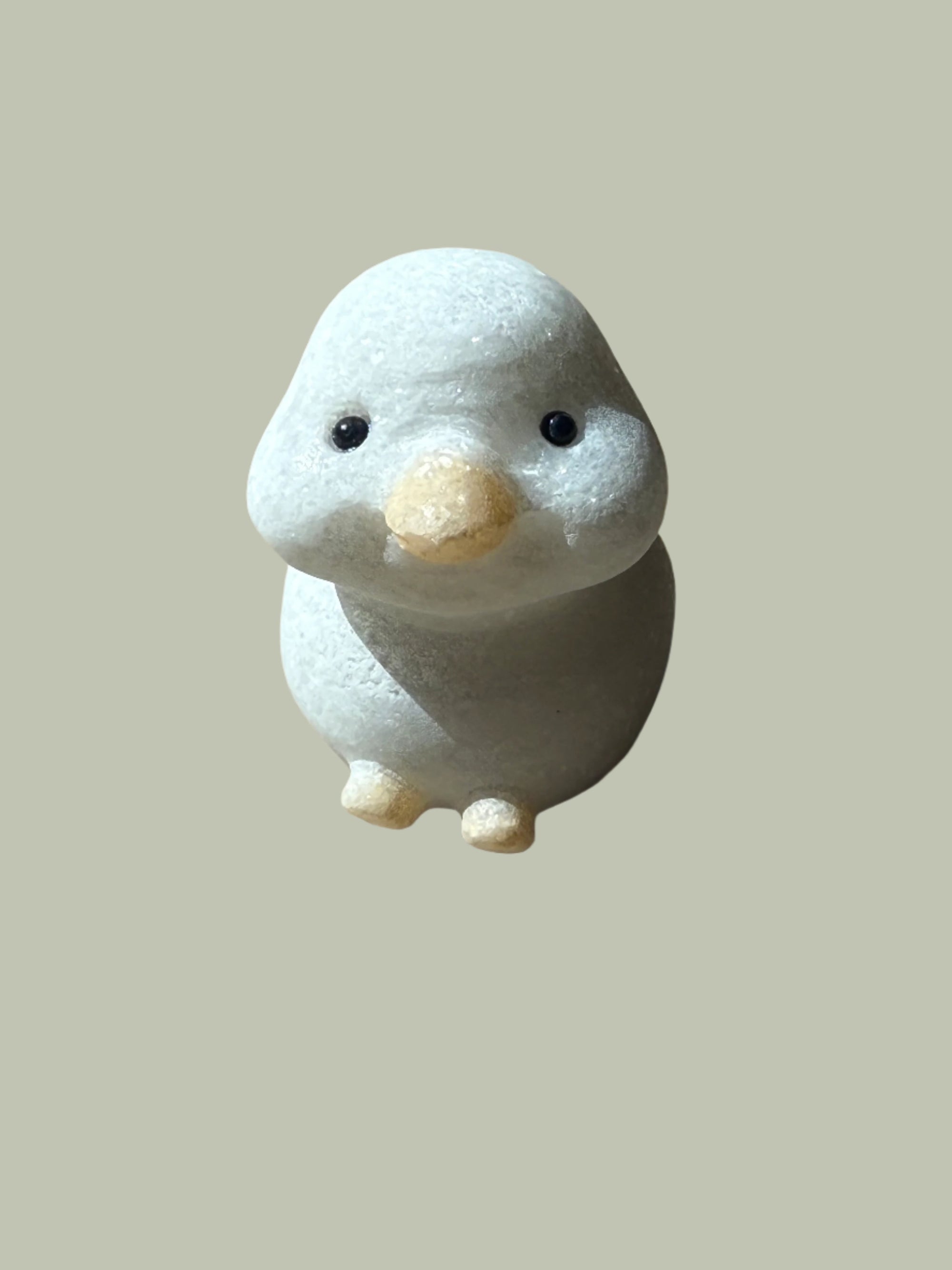 Small white figurine of a creature with a black eye and beige nose on a textured surface